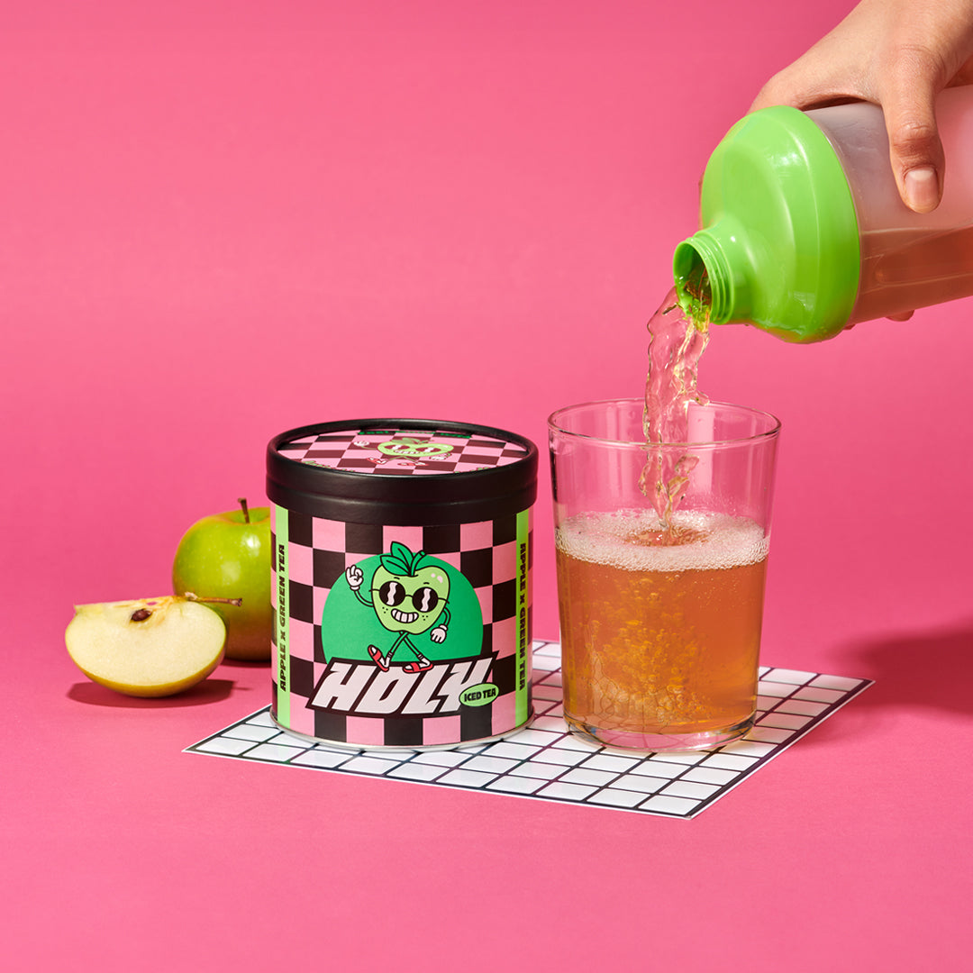 Eine Pappdose neben einem Glas, in das aus einem Shaker ein Getränk gegossen wird, vor pinkem Hintergrund.