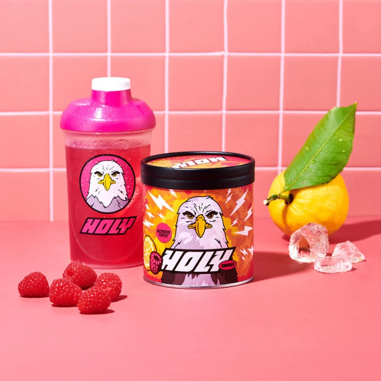 Pappdose und Shaker mit Adler-Logo auf rosa Hintergrund, umgeben von Himbeeren, einer Zitrone und Eiswürfeln.