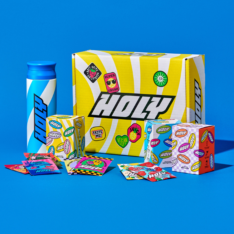 Bunte Produktverpackungen mit Shaker, Pappboxen und Probepackungen vor einem blauen Hintergrund mit dem Aufdruck "HOLY".