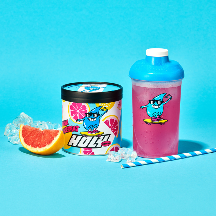 Pappdose und Shaker mit pinkem Getränk, Grapefruitscheibe, Eiswürfel und blau-weißem Strohhalm auf blauem Hintergrund.