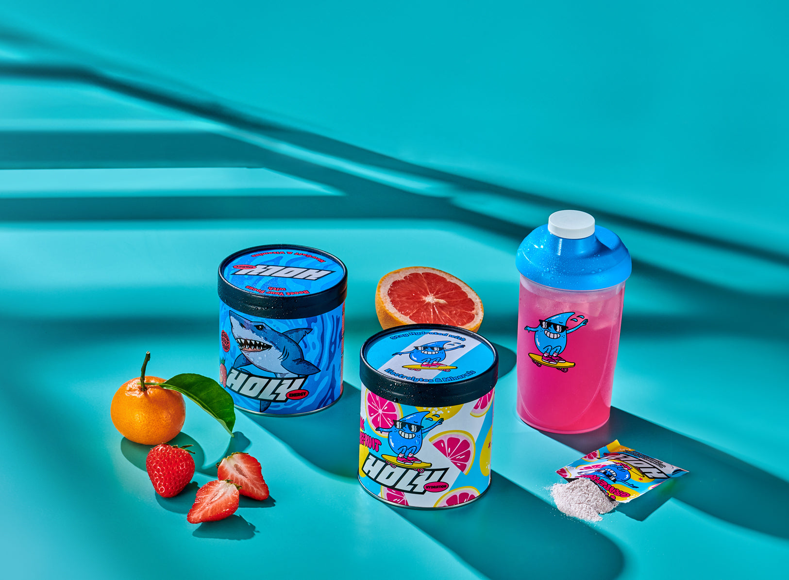 Zwei bunte Pappdosen, ein pinker Shaker, diverse Früchte und ein offenes Sachet auf türkisfarbenem Hintergrund.