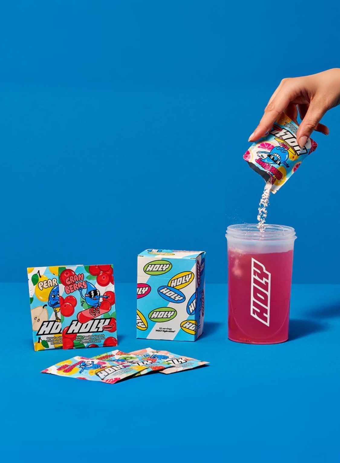 Eine Hand schüttet ein Sachet in einen Shaker, daneben stehen zwei Pappboxen und zwei weitere Sachets auf blauem Hintergrund.