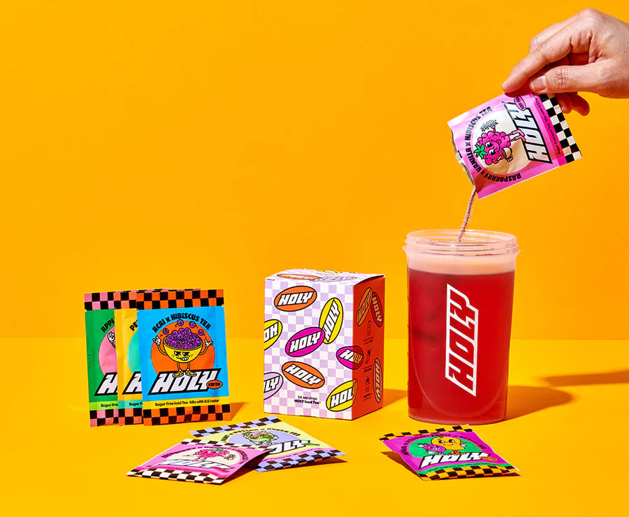 Eine Hand gießt ein rosa Getränkepulver aus einem Probepackung in einen Shaker, daneben stehen Pappdose und Probepackungen.