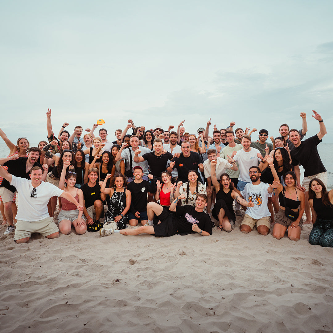 Eine große Gruppe von Menschen posiert fröhlich am Strand für ein Foto.