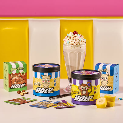 Pappdosen und Probepackungen mit bunten Designs stehen neben einem Milchshake vor einer gelben und pinken Wand.