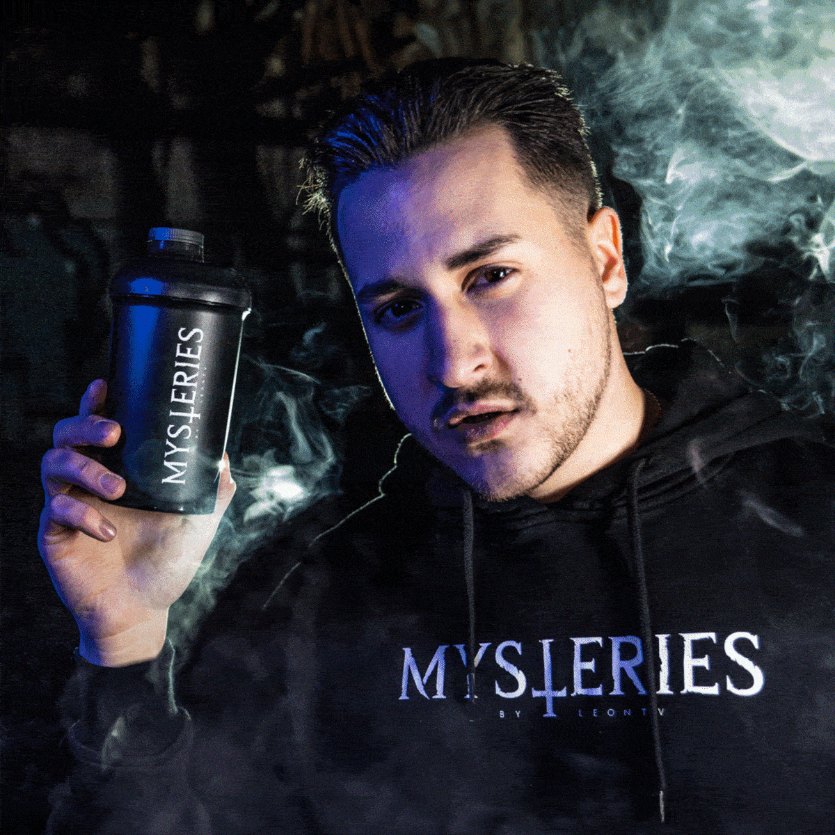 Person in schwarzem Hoodie hält einen Shaker mit "MYSTERIES"-Aufdruck, umgeben von Rauch.